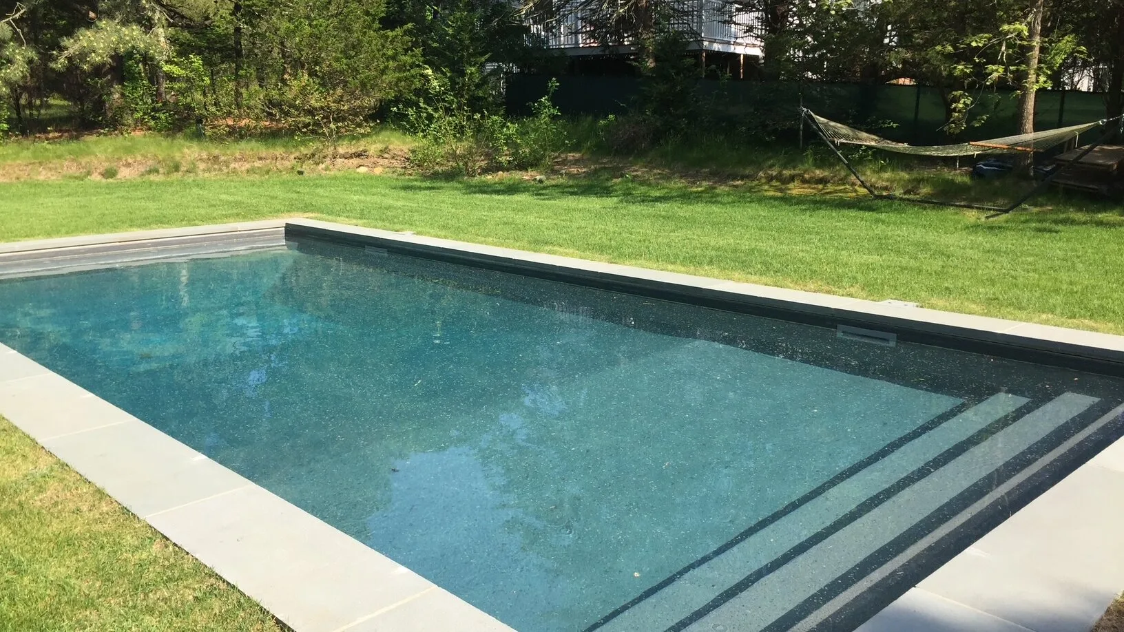 Una piscina al aire libre está junto a un césped y árboles.