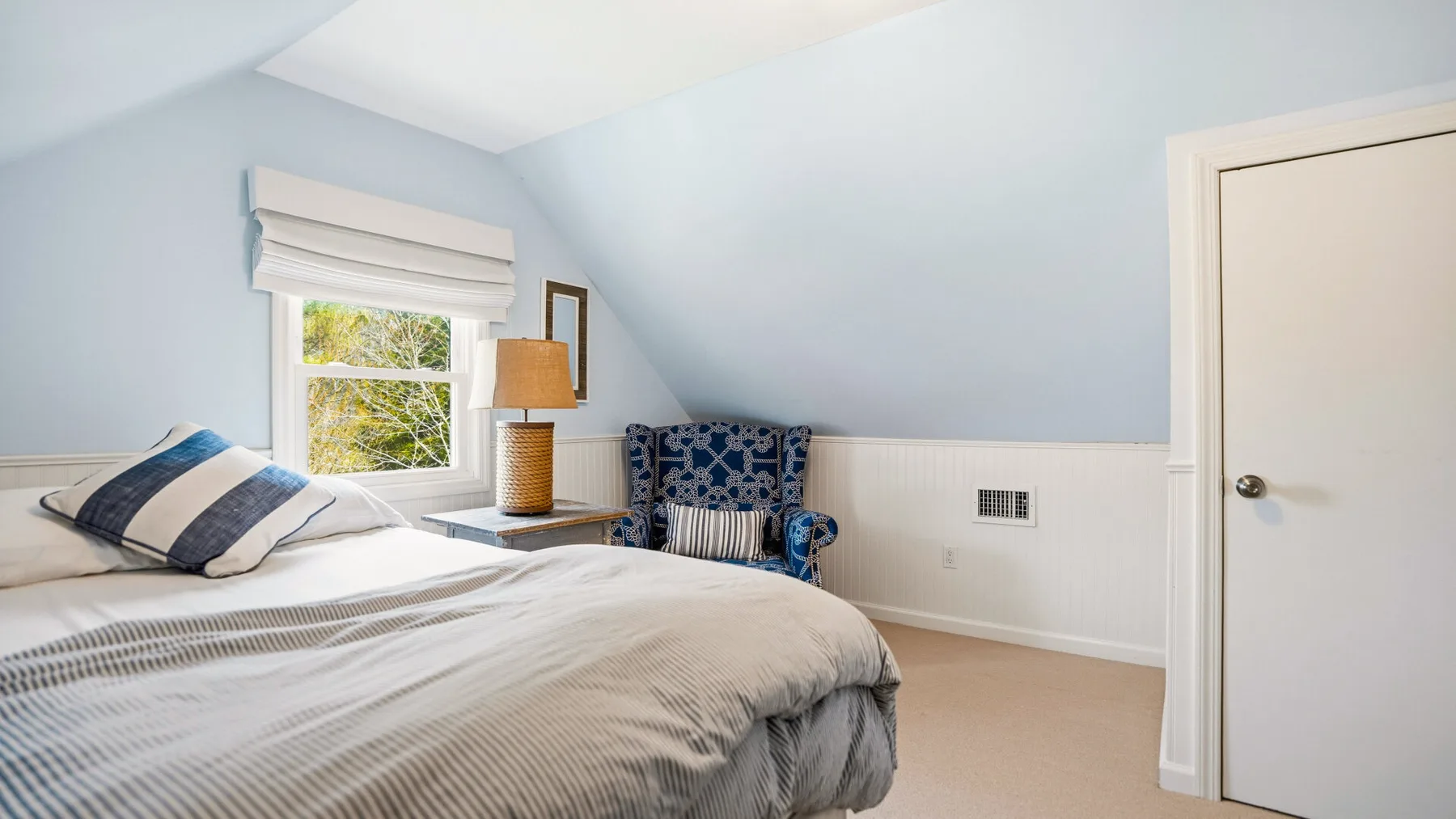 Un dormitorio luminoso con una cama, una ventana y un sillón azul.