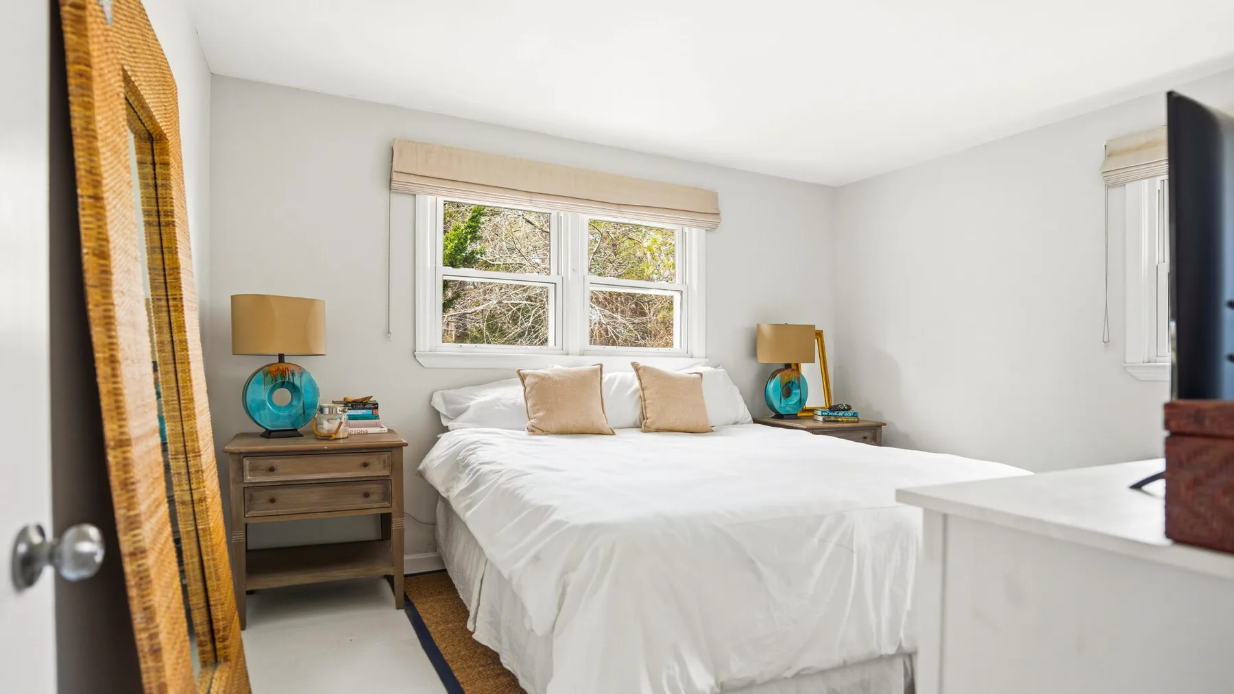 Un dormitorio luminoso con una cama bajo una ventana y mesitas de noche.