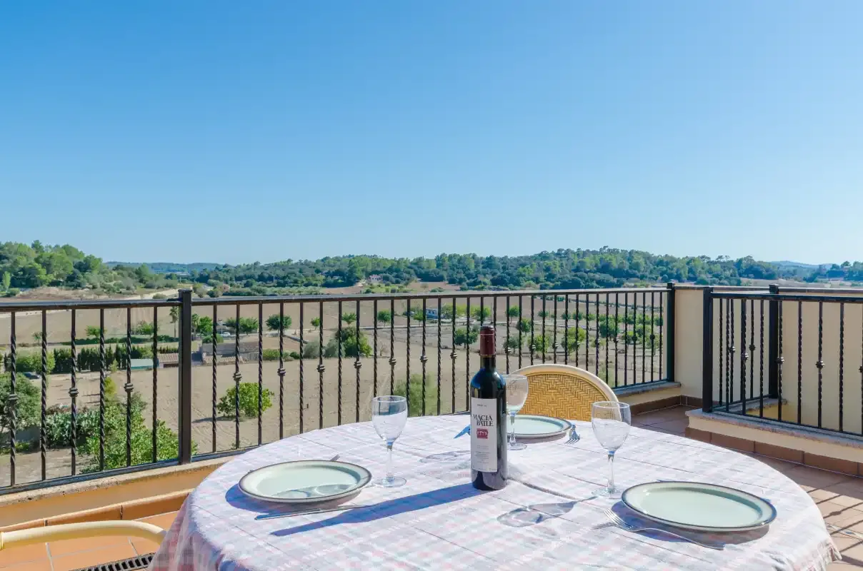 A balcony dining table overlooks open fields and a tree-lined horizon.