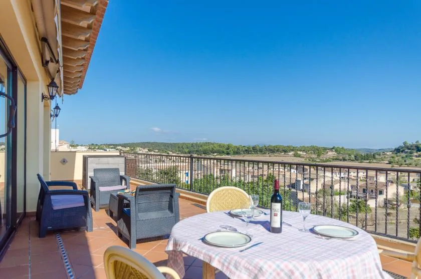 A terrace dining area overlooks a broad landscape beneath a clear blue sky.