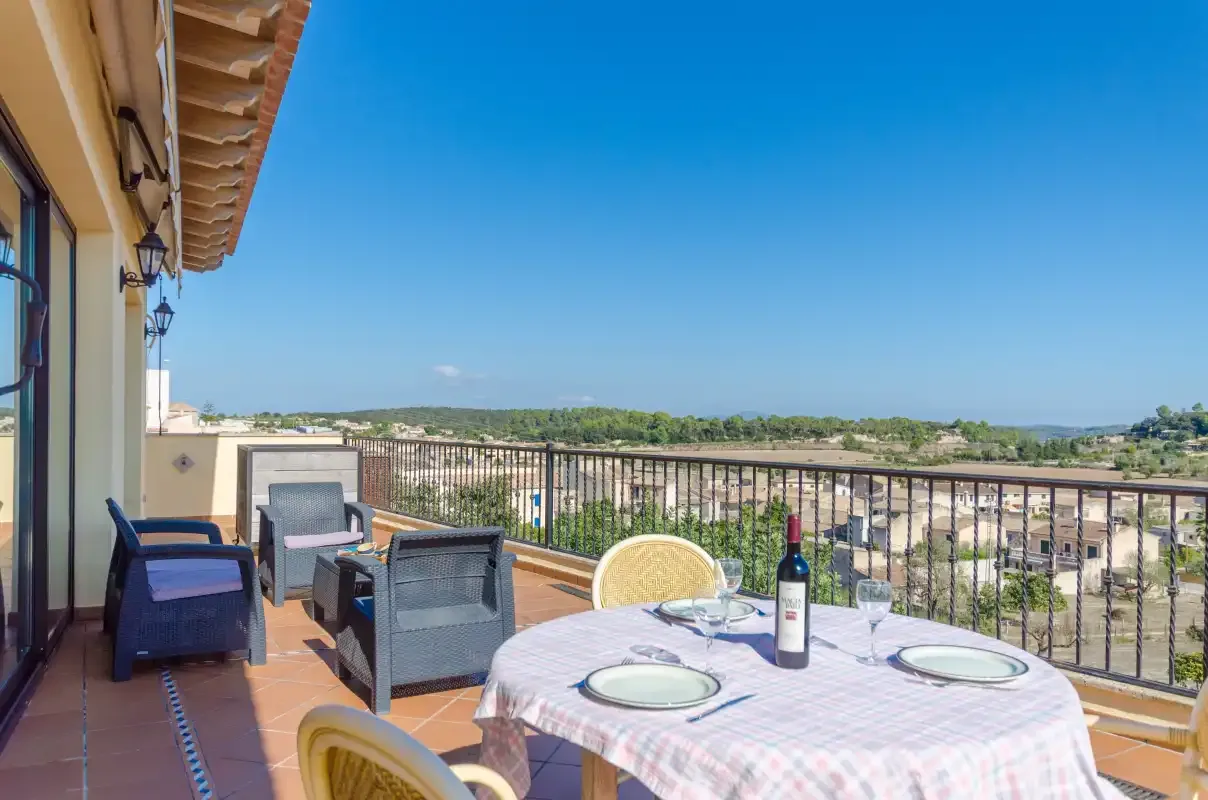 A sunny terrace has outdoor seating, a dining table, and views across the surrounding landscape.
