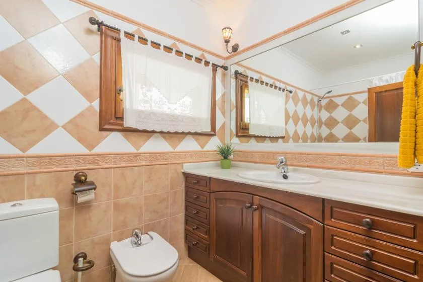 A tiled bathroom with a wooden vanity, sink, and toilet.