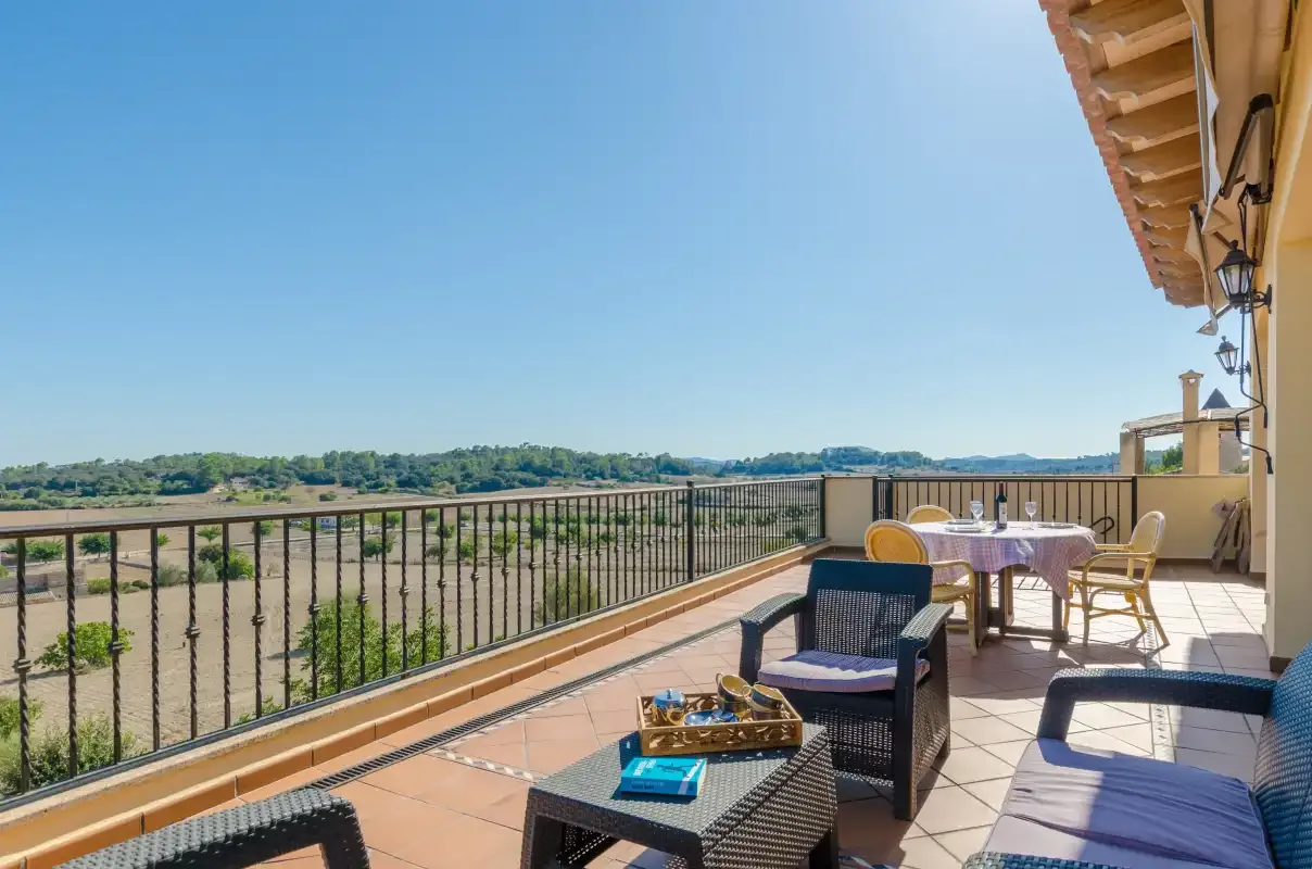 A furnished terrace overlooks a green landscape beneath a clear sky.
