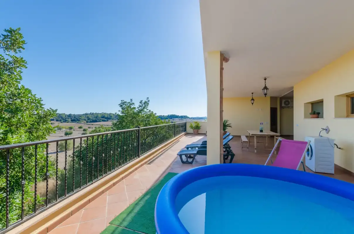 A covered terrace overlooks green fields, with a blue inflatable pool in the foreground.