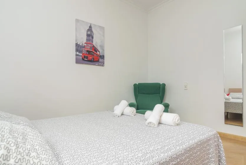 A bedroom with a bed, folded towels, and a green chair.