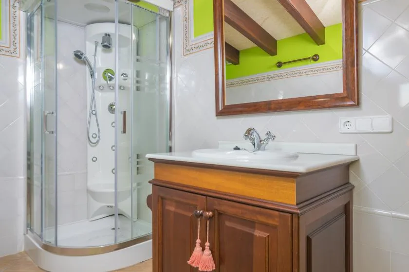 A tiled bathroom with a glass shower and a wooden vanity beneath a mirror.
