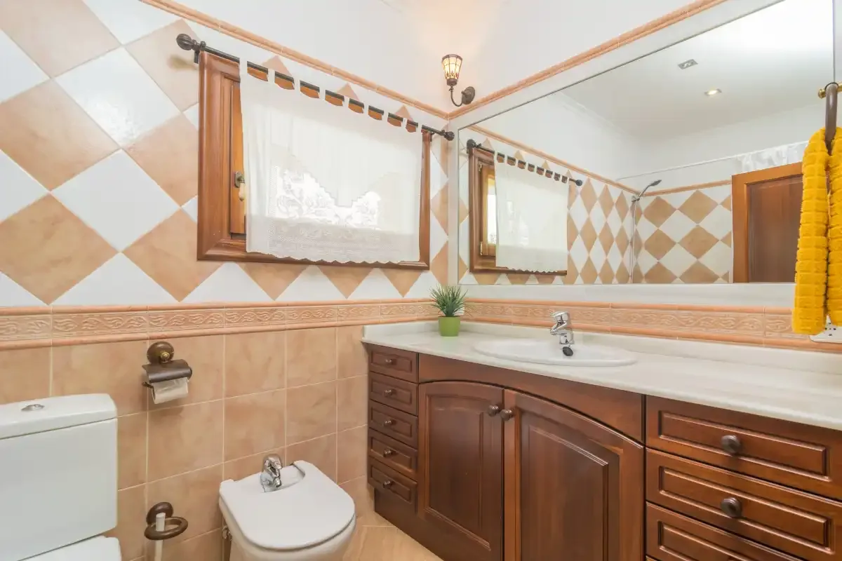 A tiled bathroom with a wooden vanity, sink, and large mirror.