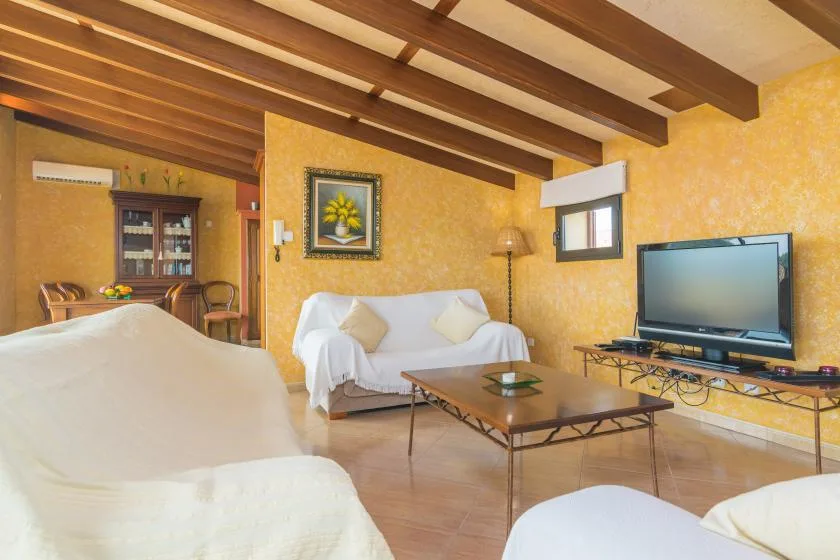 Una sala de estar con asientos, una mesa de centro y un televisor bajo vigas de madera.