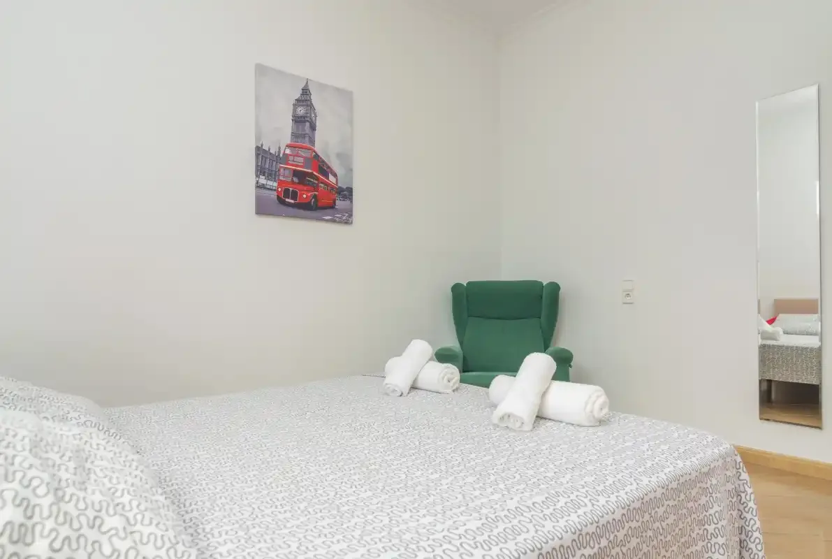 A bedroom with a patterned bedspread, green chair, and wall art.