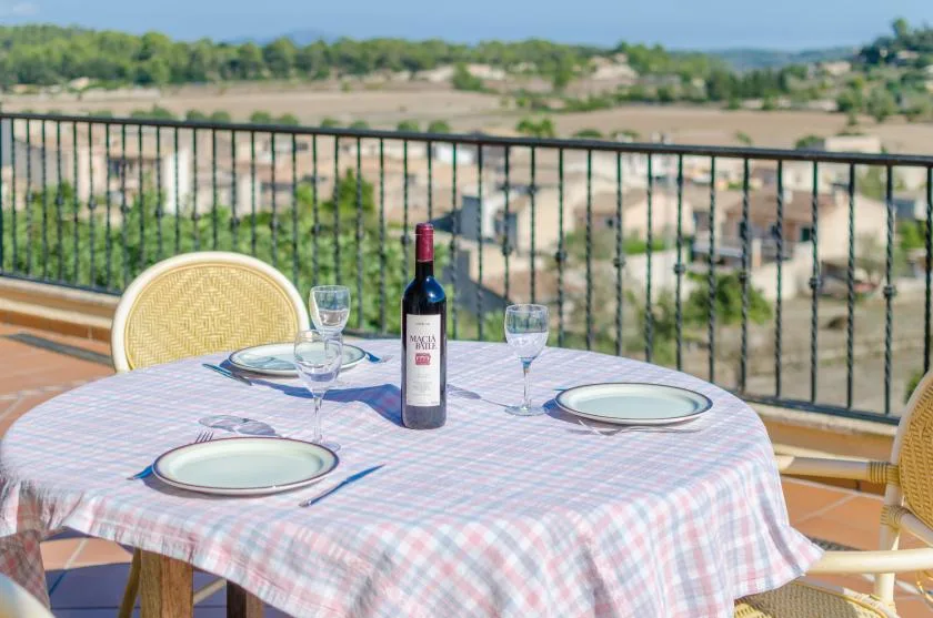 A terrace dining table is set with plates and glasses beside a railing.