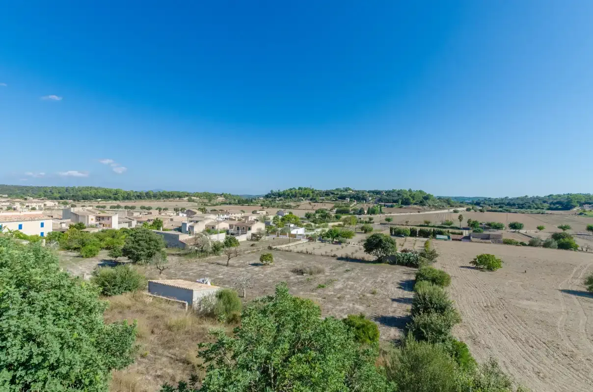 A broad rural landscape with scattered buildings and fields beneath a clear blue sky.