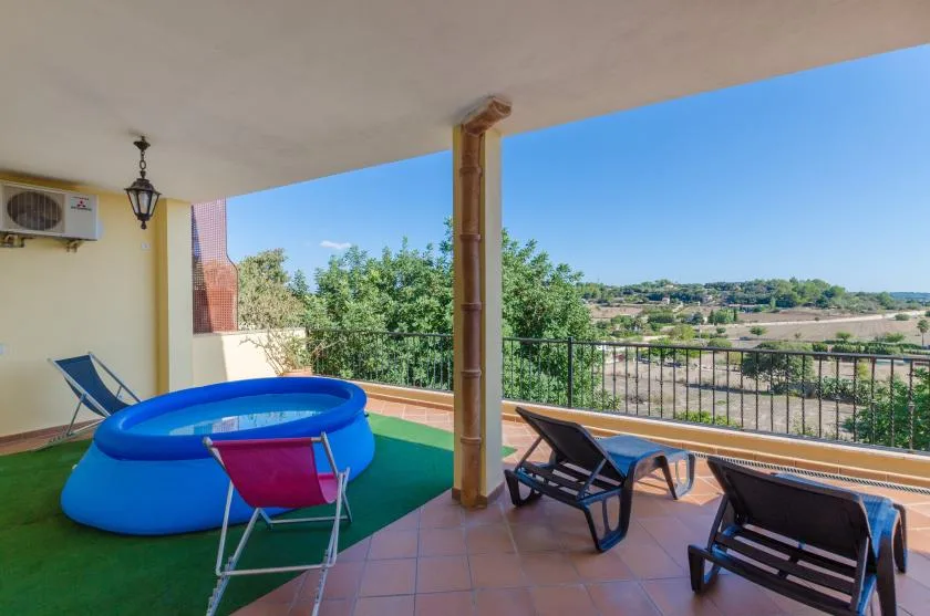 A covered terrace with a small inflatable pool and outdoor seating overlooks a green landscape.