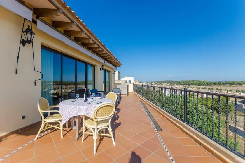 A sunny outdoor terrace with a dining table and railing overlooking the landscape.
