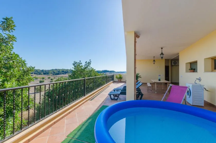A covered terrace with a blue inflatable pool and seating overlooks a green landscape.