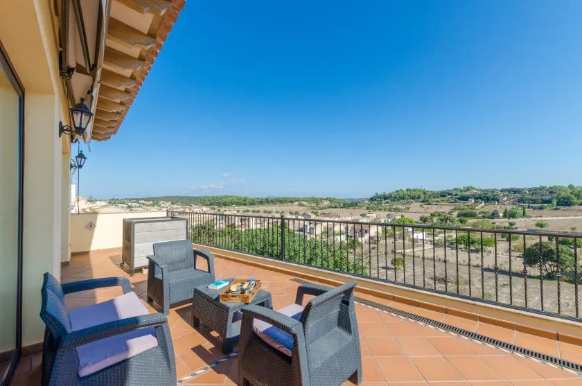 A furnished terrace overlooks a green landscape beneath a clear blue sky.
