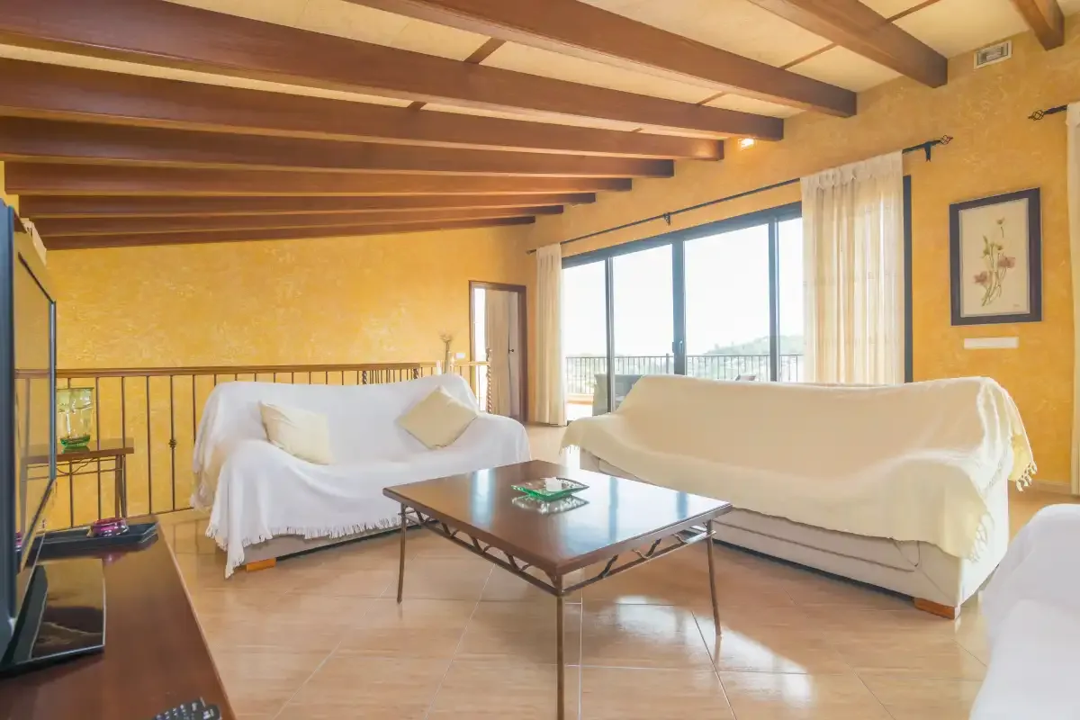A bright living room with covered seating, a coffee table, and large windows.