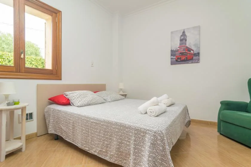 A bedroom with a double bed, folded towels, and a window overlooking greenery.