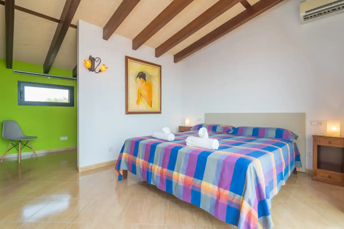 A bedroom with a colorful striped bedspread and exposed ceiling beams.