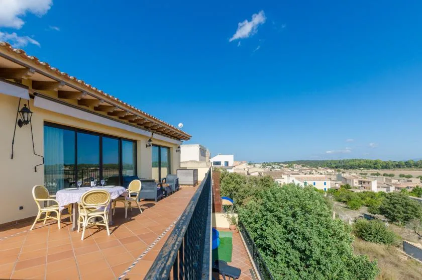 A sunny terrace with outdoor seating overlooks a green landscape and distant buildings.
