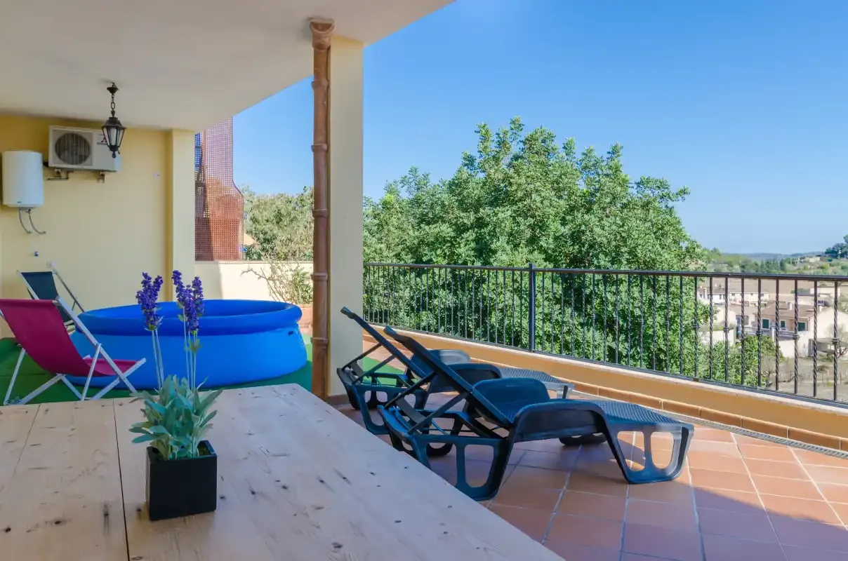 A sunny terrace with lounge seating, a blue pool, and views of trees beyond the railing.