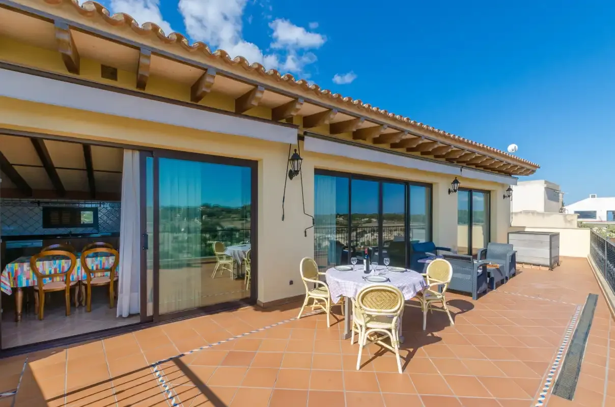 A sunny terrace with outdoor seating and glass doors opening onto an indoor dining area.