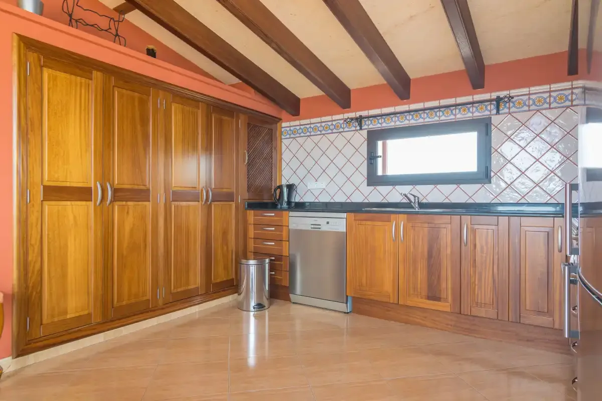 A kitchen with wooden cabinets, a tiled backsplash, and exposed ceiling beams.