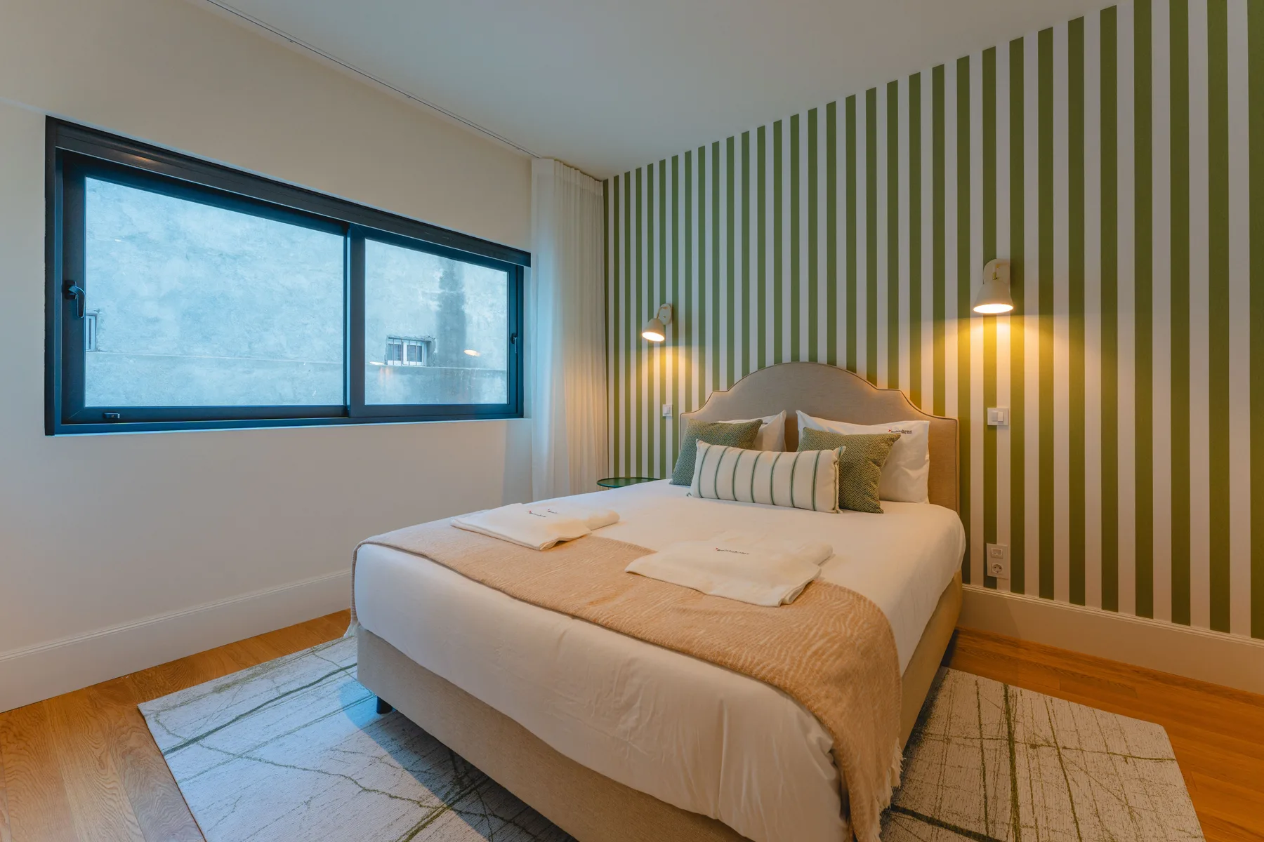 Un dormitorio con una cama bien tendida frente a una pared decorativa a rayas.