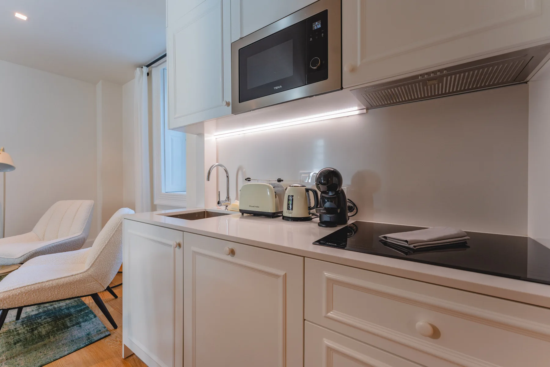 Una pequeña cocina con electrodomésticos sobre la encimera junto a una zona de estar.