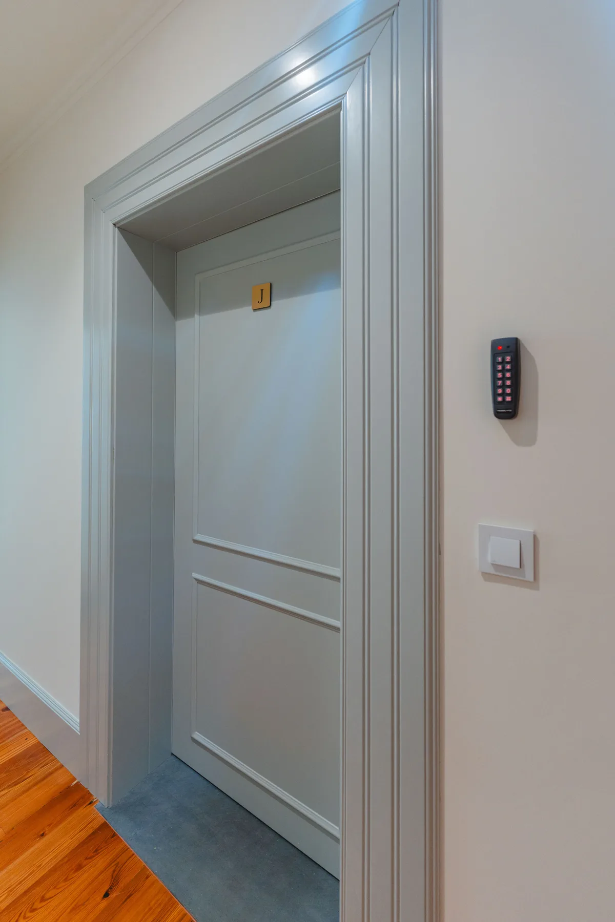 Un pasillo con una puerta gris cerrada y un teclado en la pared.