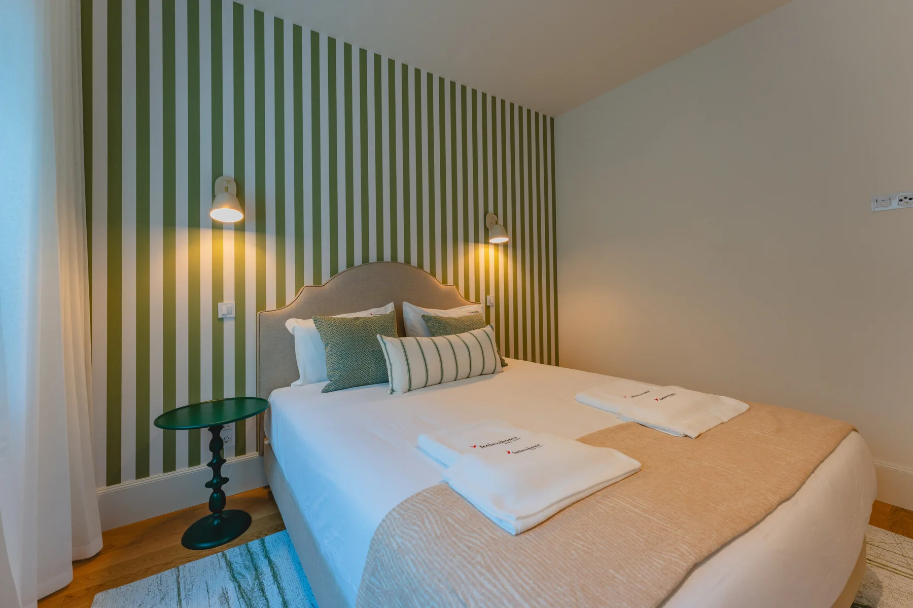 Un dormitorio con una cama bien hecha junto a una pared decorativa de rayas verdes.