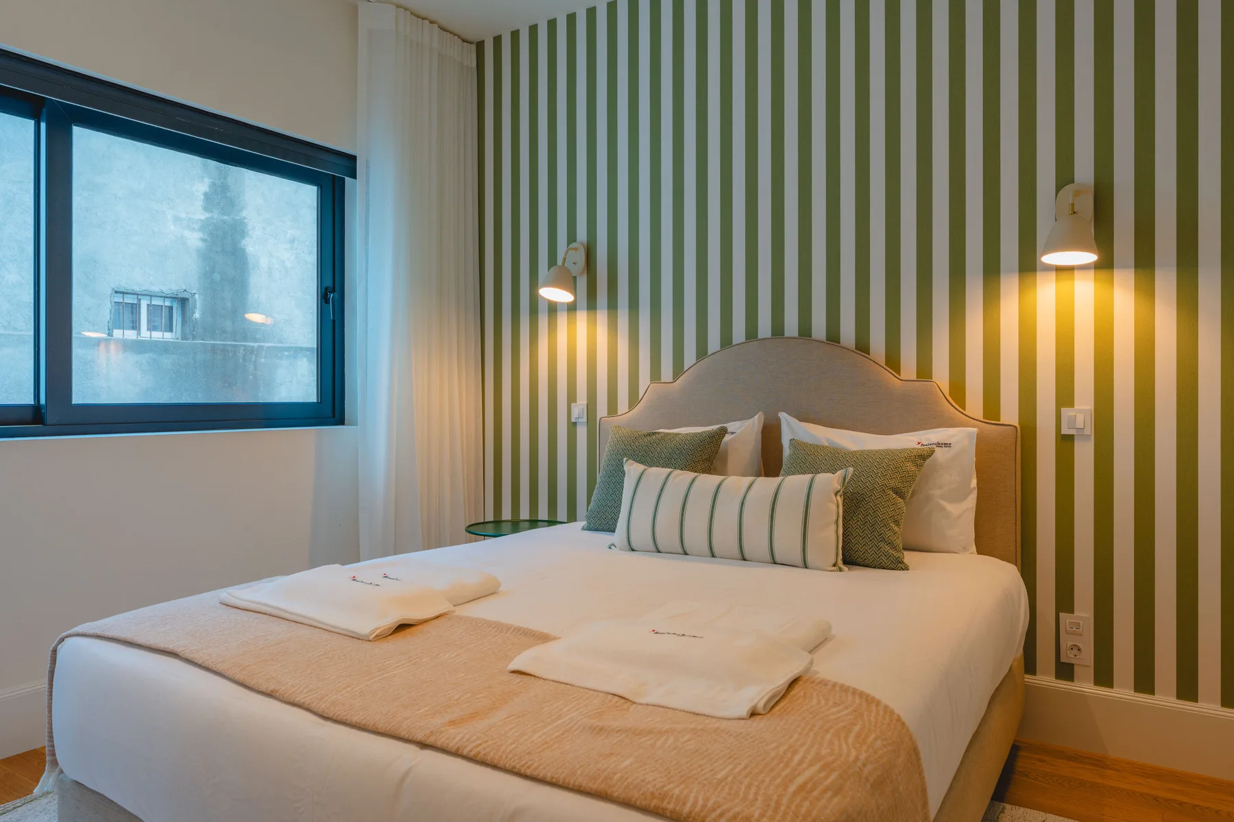 Un dormitorio con una cama, una pared a rayas y una ventana.