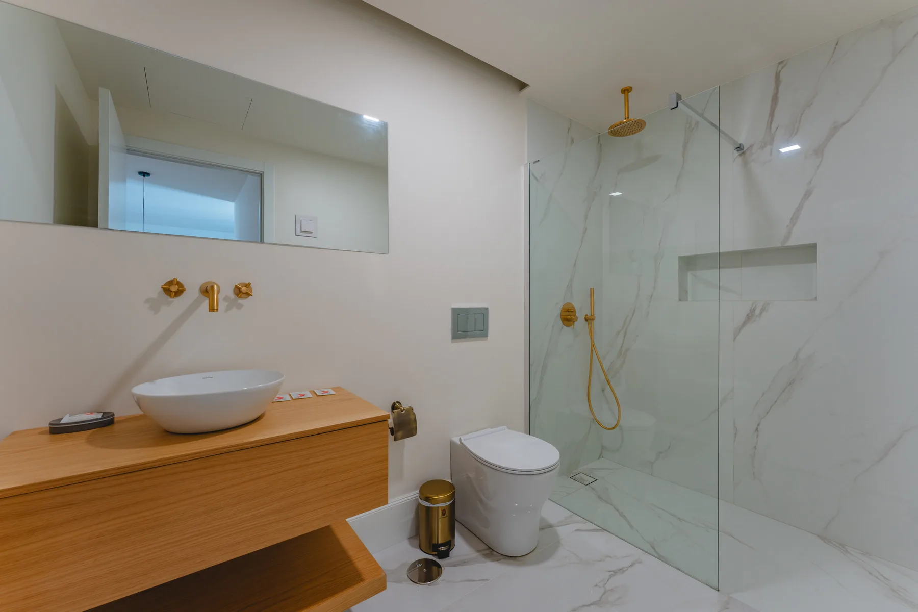 Un baño moderno con lavabo de madera, lavamanos, inodoro y ducha de cristal.