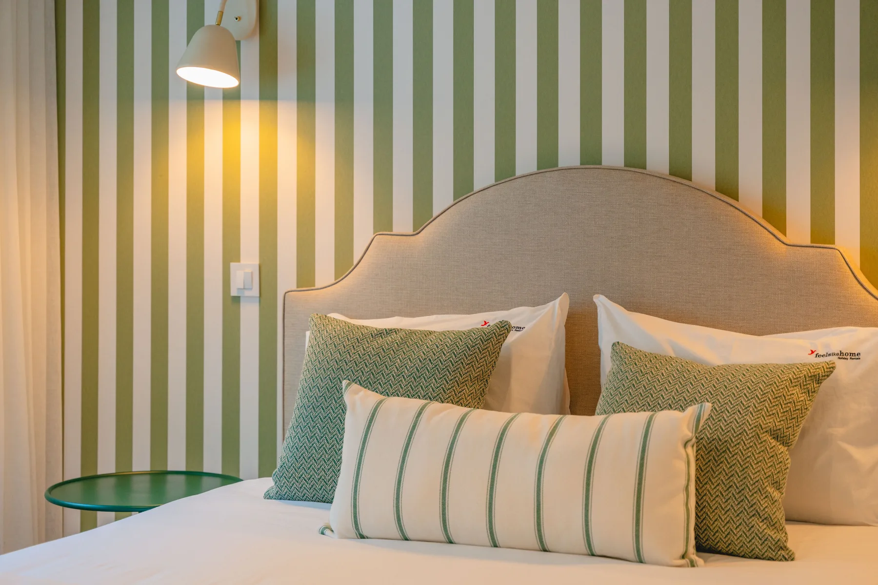 Dormitorio con una cama, papel pintado a rayas y una lámpara de lectura en la pared.