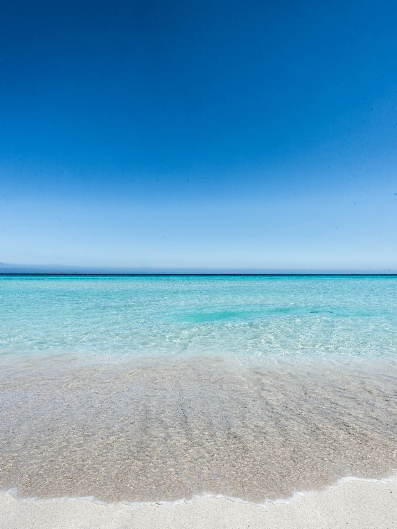 Una orilla tranquila con agua turquesa clara bajo un cielo azul.