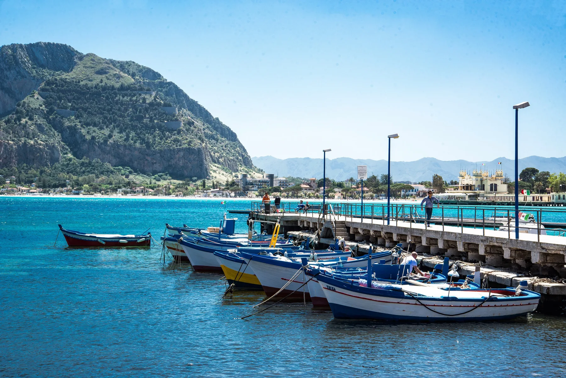 Hay barcos amarrados junto a un muelle, con una montaña al otro lado de la bahía.