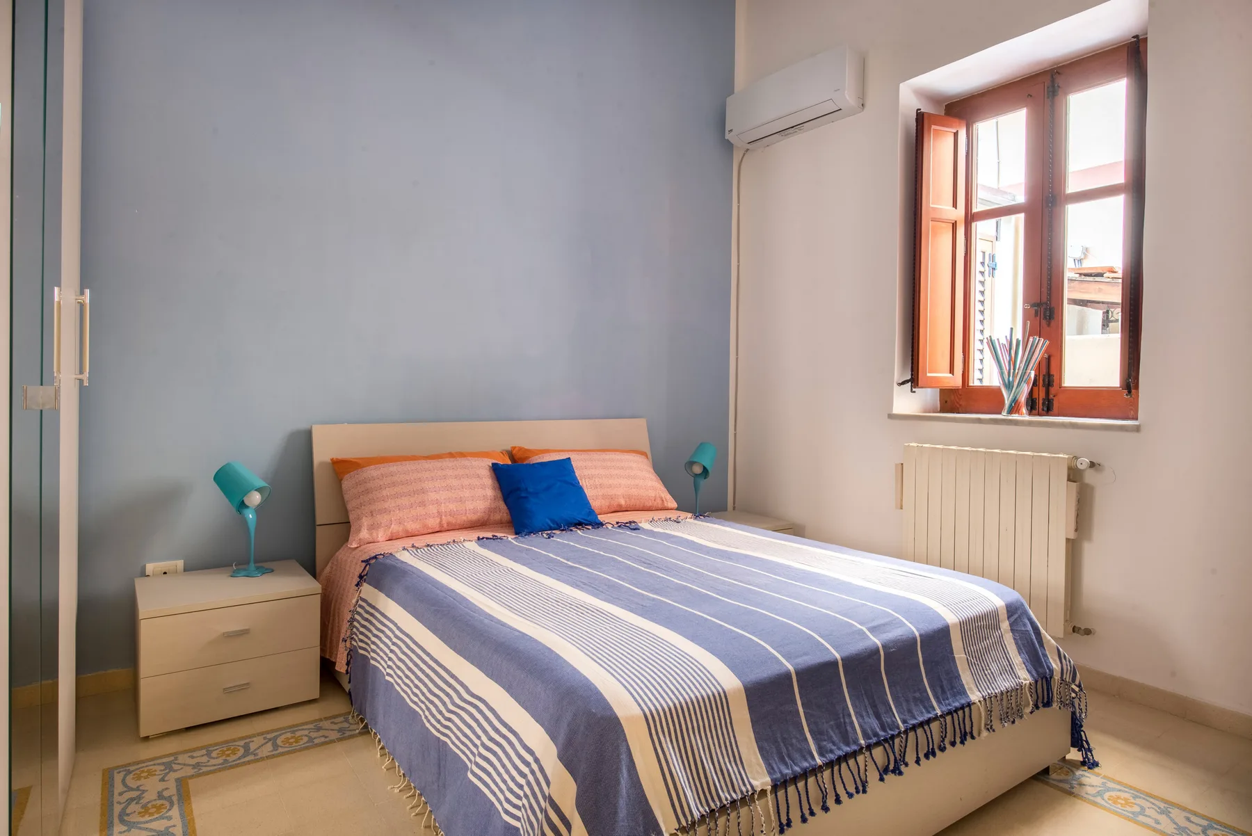 Un dormitorio con una colcha a rayas, mesitas de noche y una ventana.