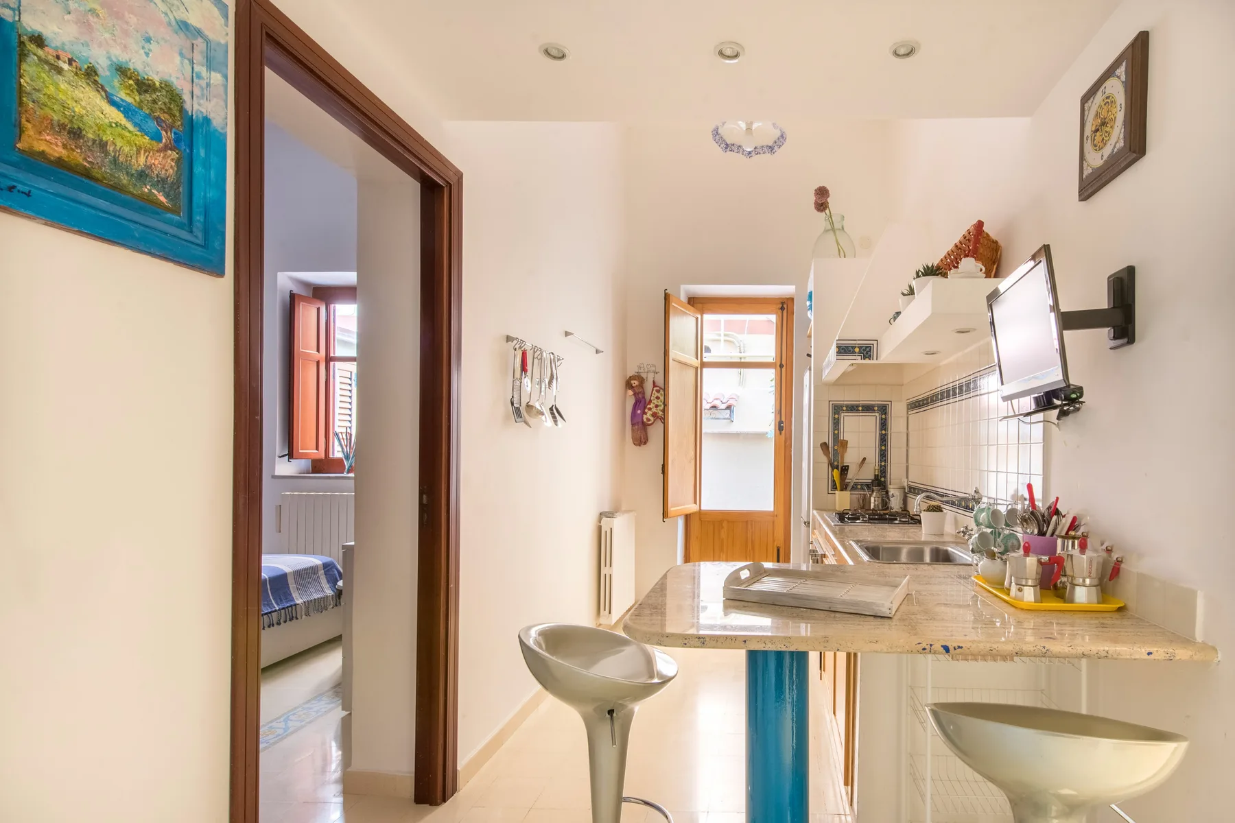 Una cocina luminosa con encimera, fregadero y televisor en la pared.