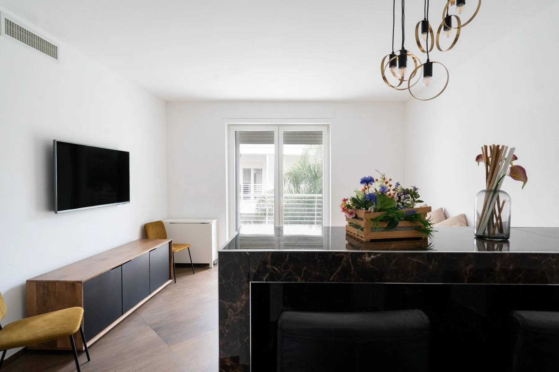 A bright modern living area with a television, dark cabinetry, and sliding glass doors.