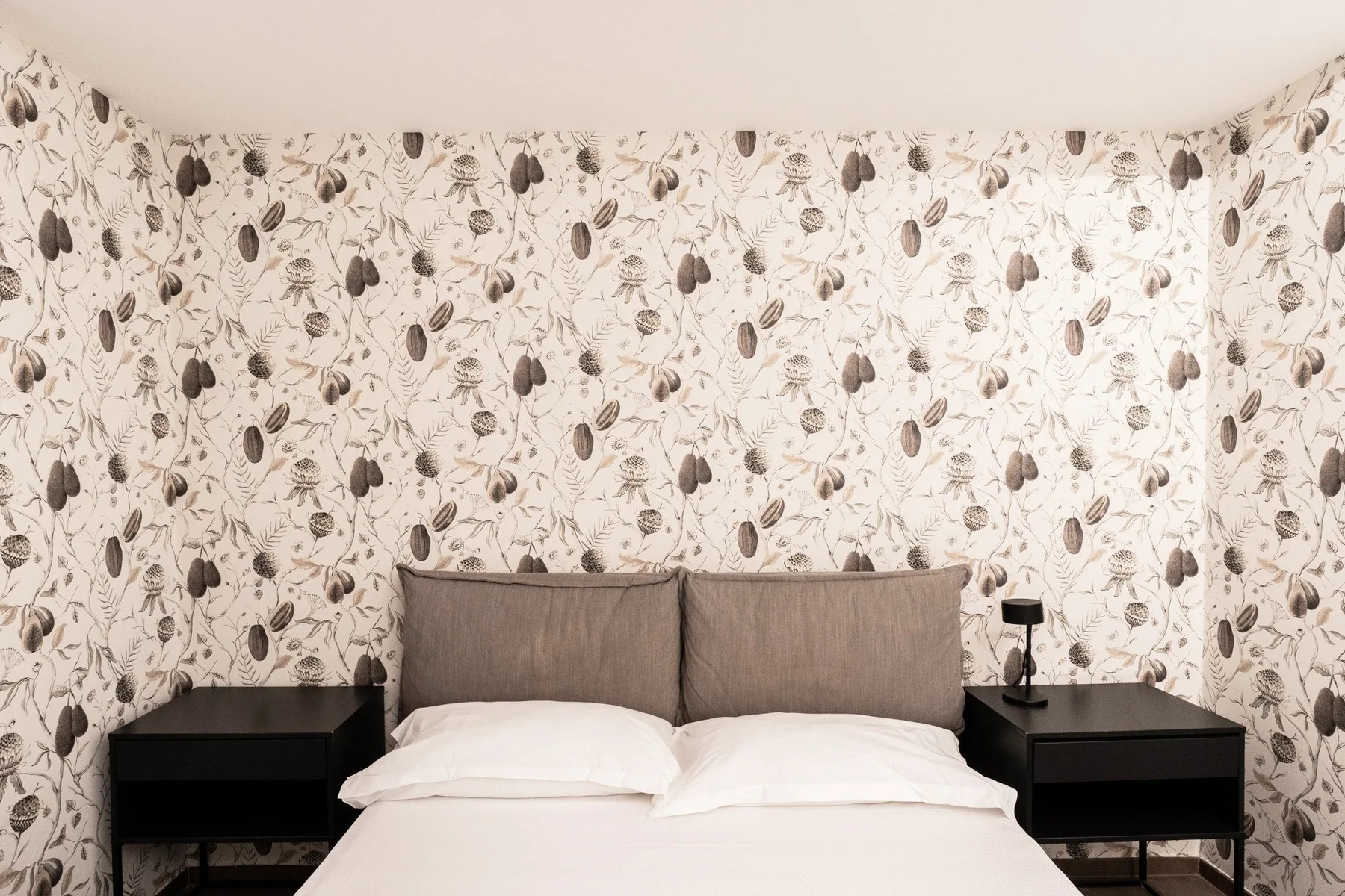 A bedroom with a bed, black bedside tables, and patterned wallpaper.