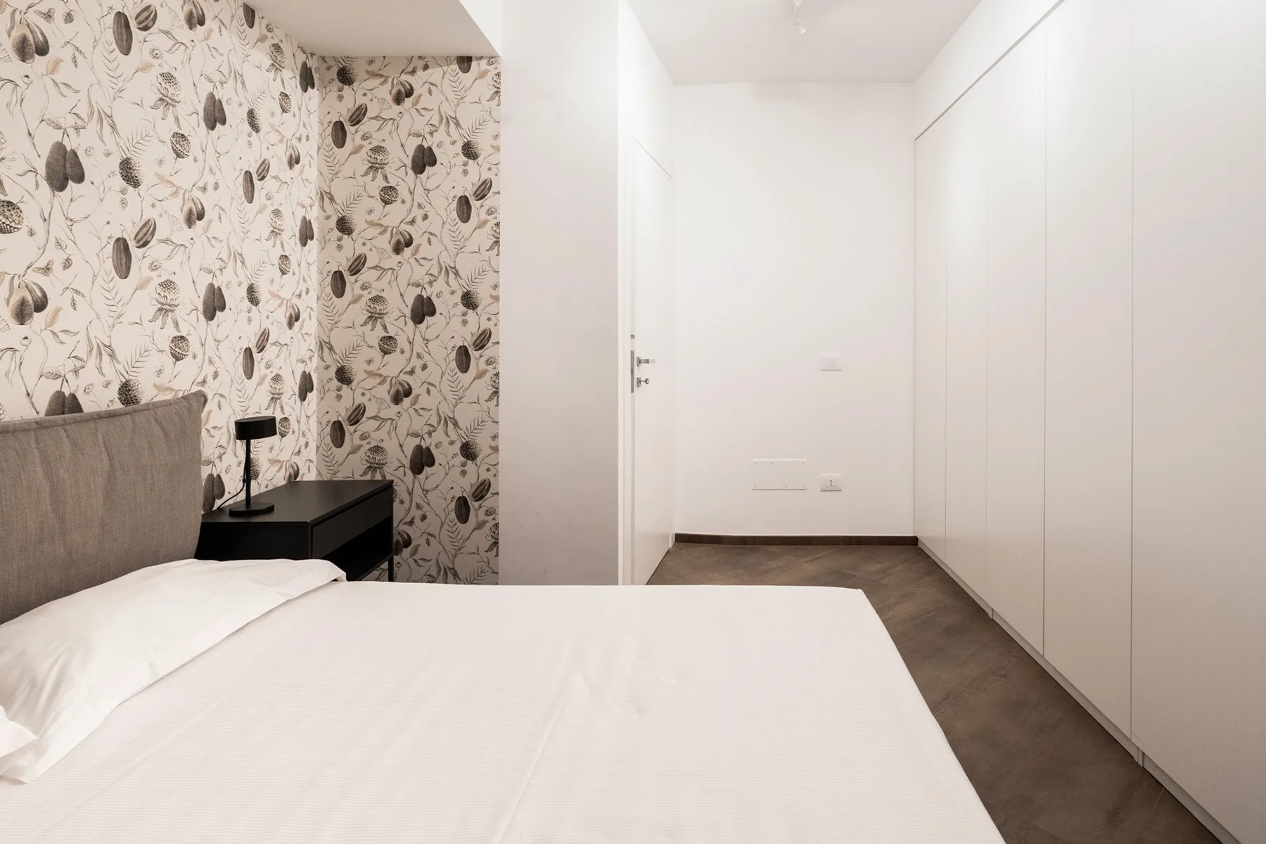 A bedroom with a bed, patterned wallpaper, and built-in wardrobes.