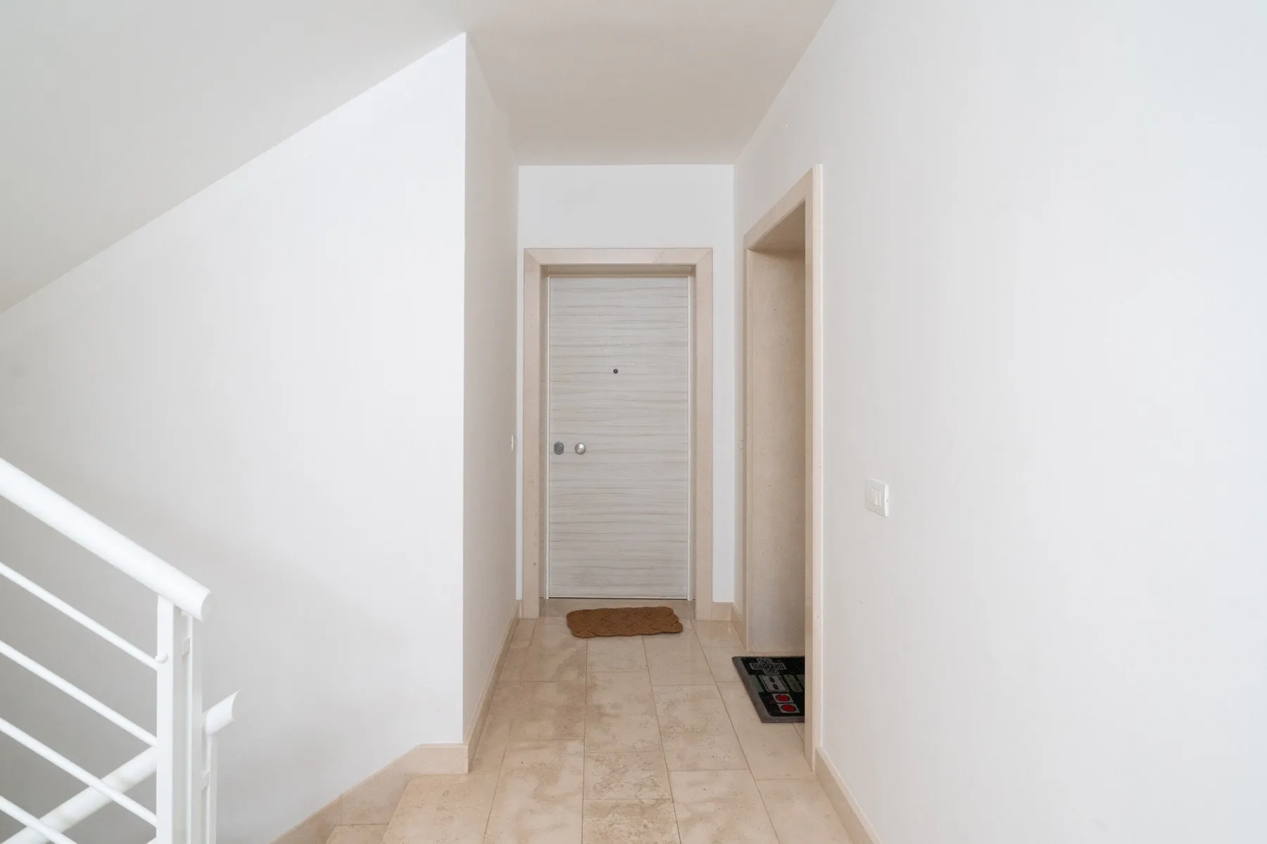 A bright hallway with a closed door and a staircase railing.