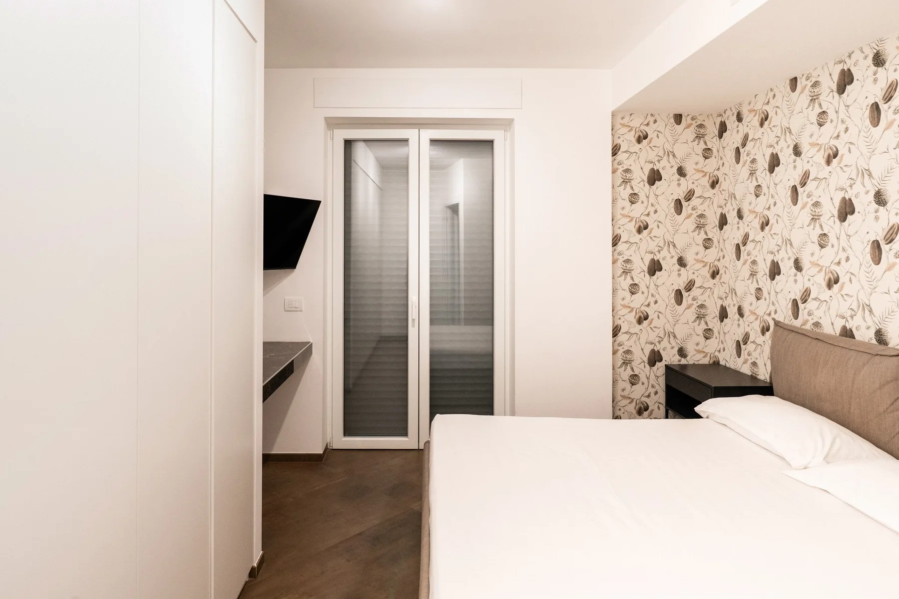 A bedroom with a neatly made bed beside a patterned accent wall.