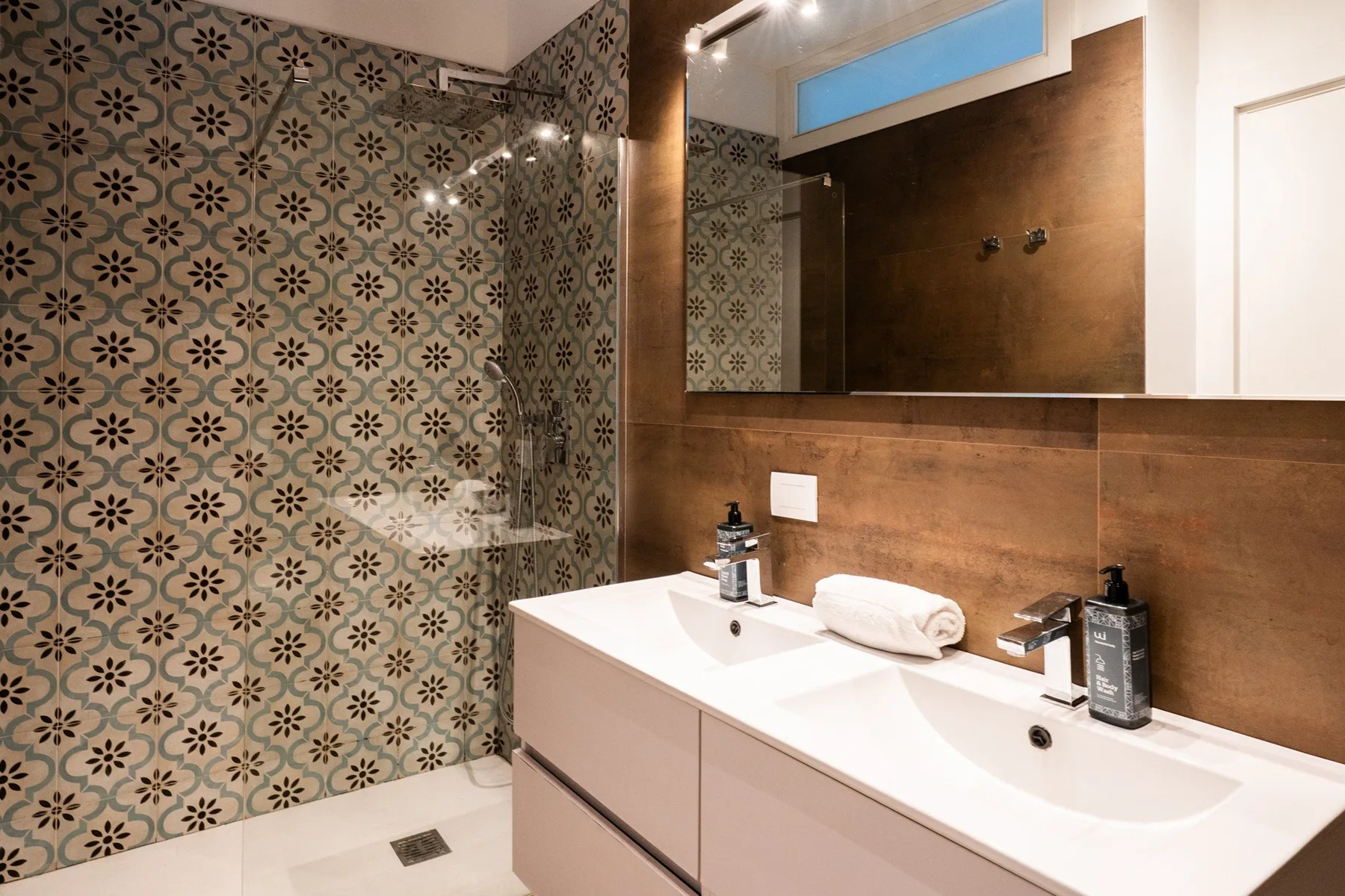 A bathroom with a patterned shower area and a double-sink vanity.
