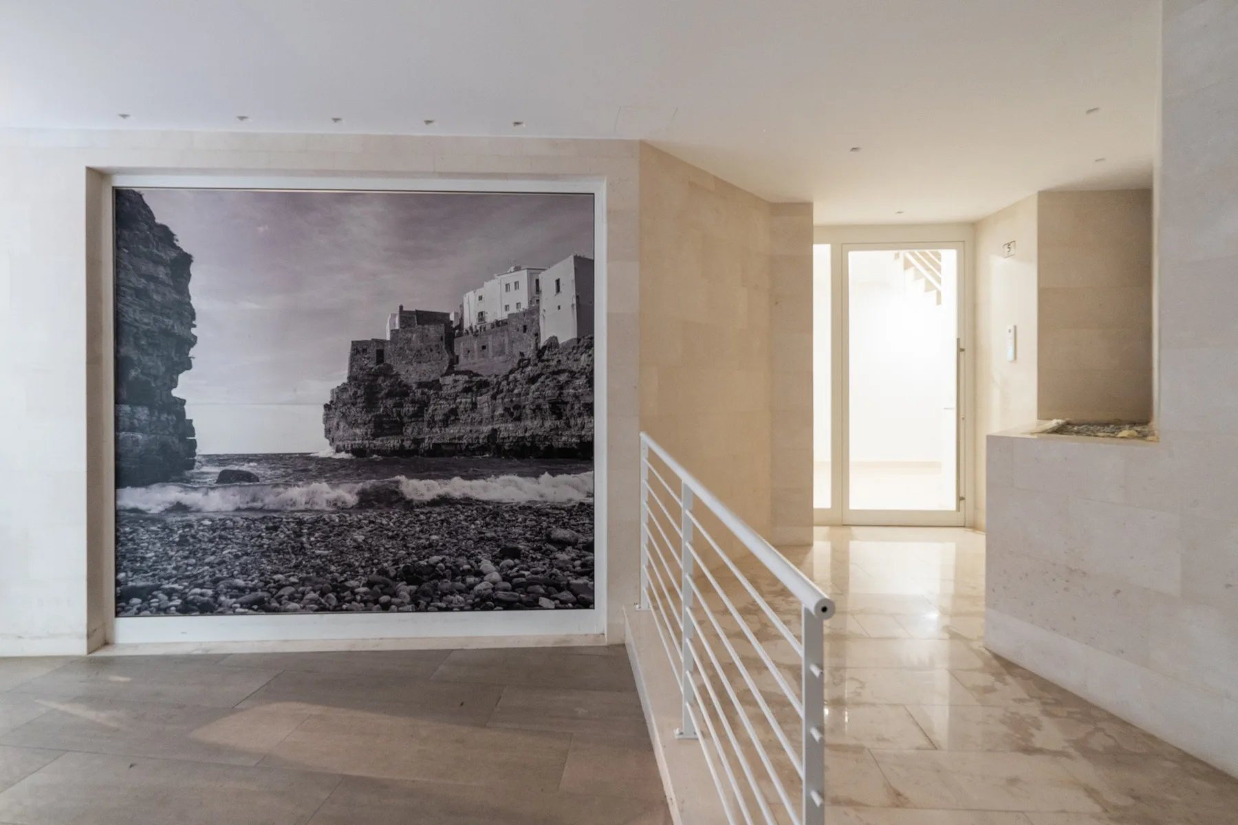 A bright interior hallway features a large black-and-white coastal photograph.