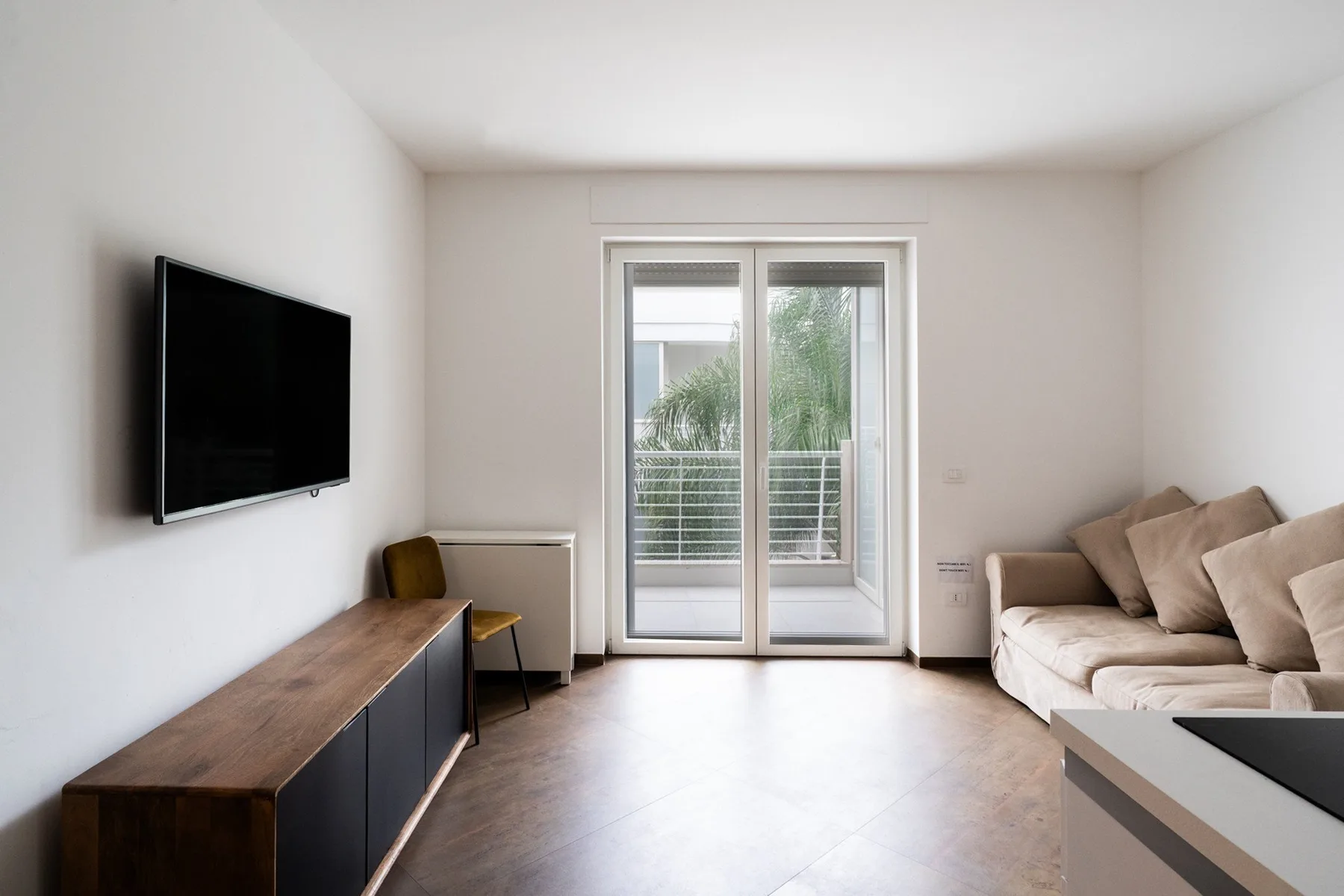 A bright living room with a television, seating, and glass doors opening to a balcony.