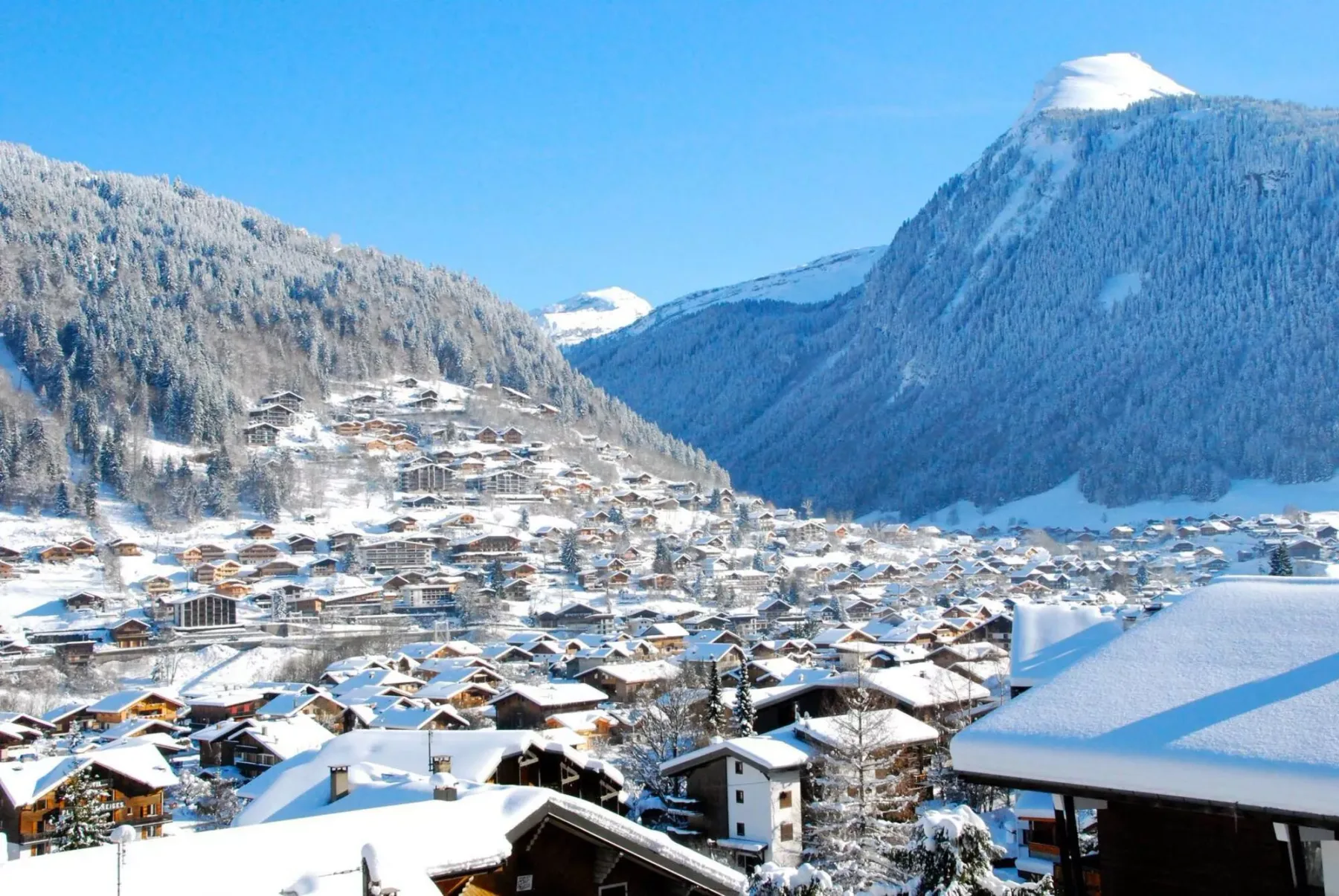 Un pueblo cubierto de nieve ocupa el valle bajo laderas boscosas.