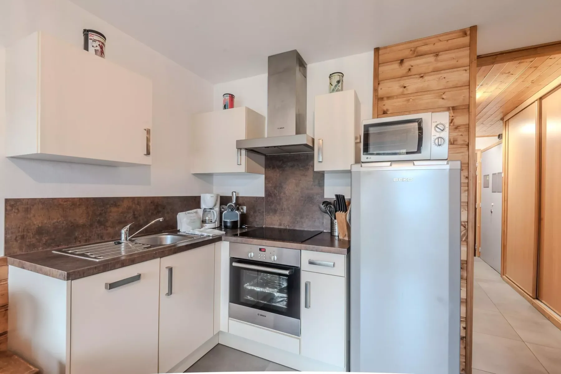 A compact kitchen with white cabinets, dark countertops, and a stainless-steel refrigerator.