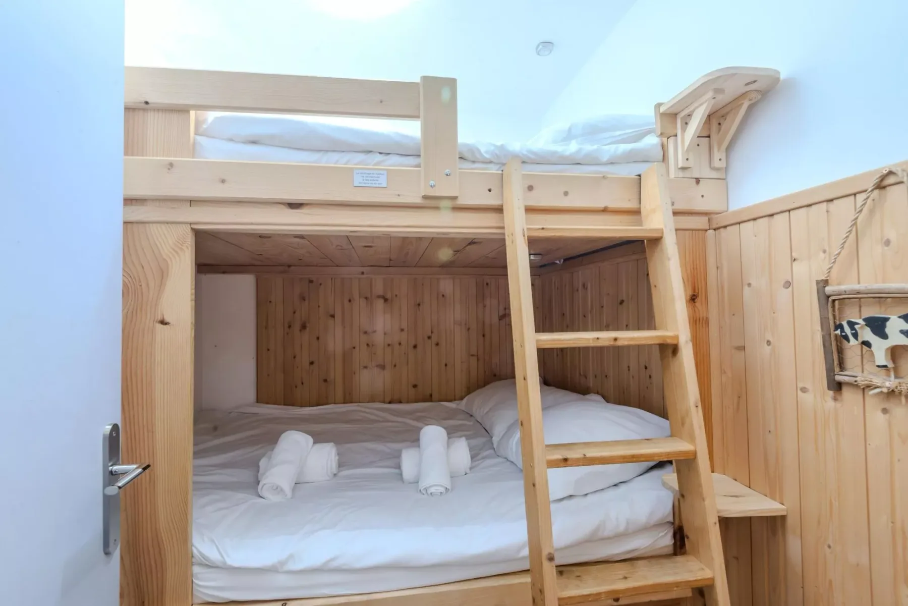 Una litera de madera con ropa de cama blanca y una escalera en una pequeña zona para dormir.