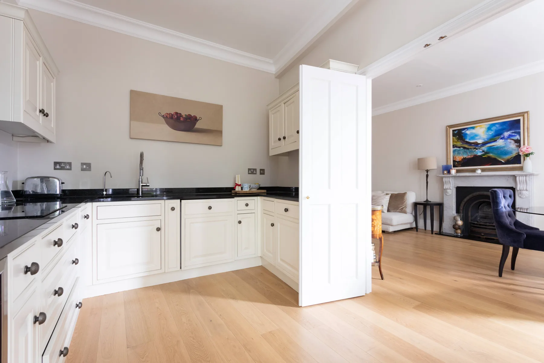 A bright kitchen with white cabinetry opens into a living area with a fireplace.